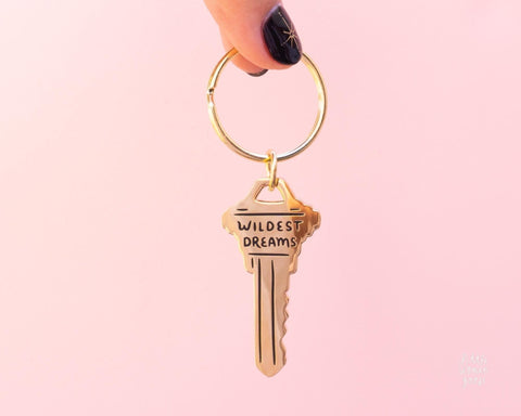 Cute gold metal keychain in the shape of a key with the text " Wildest Dreams" engraved on the key